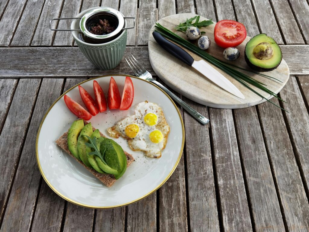 Breakfast setup with avocado toast, quail eggs, and fresh tomatoes on a rustic wooden table.