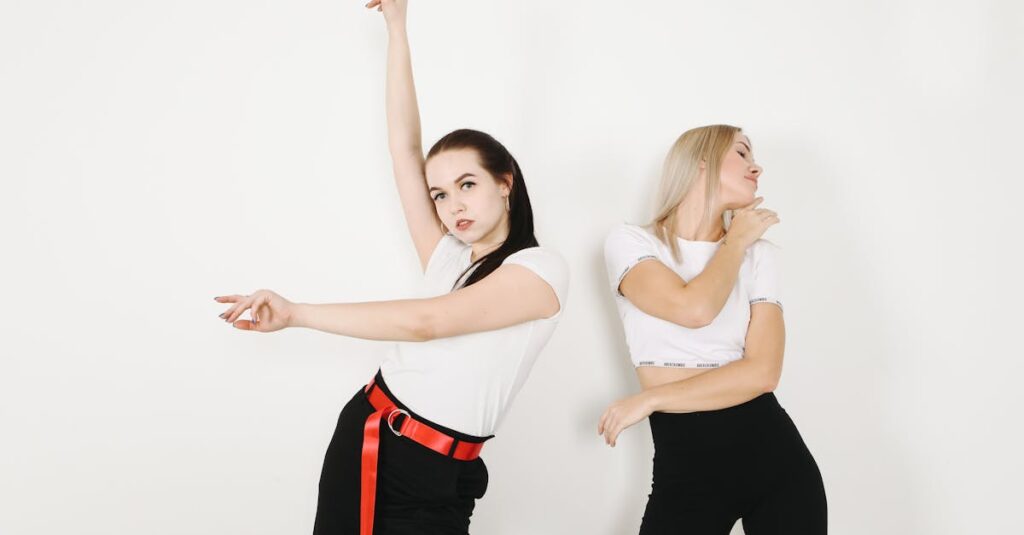 Thoughtful slim brunette with red belt raising hand while dancing close to blond female with closed eyes touching chin near white wall