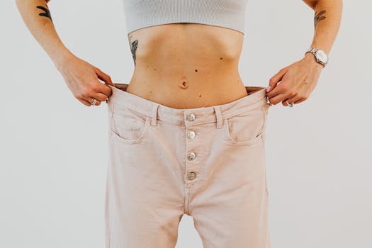 Close-up of a woman holding oversized pants at her waist, showcasing significant weight loss.