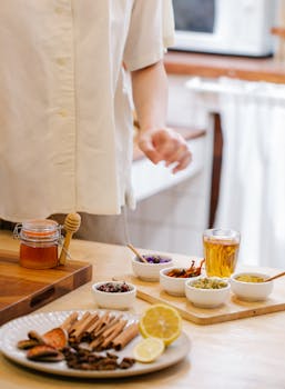 A close-up of ingredients for herbal tea, featuring bowls of spices and a jar of honey.