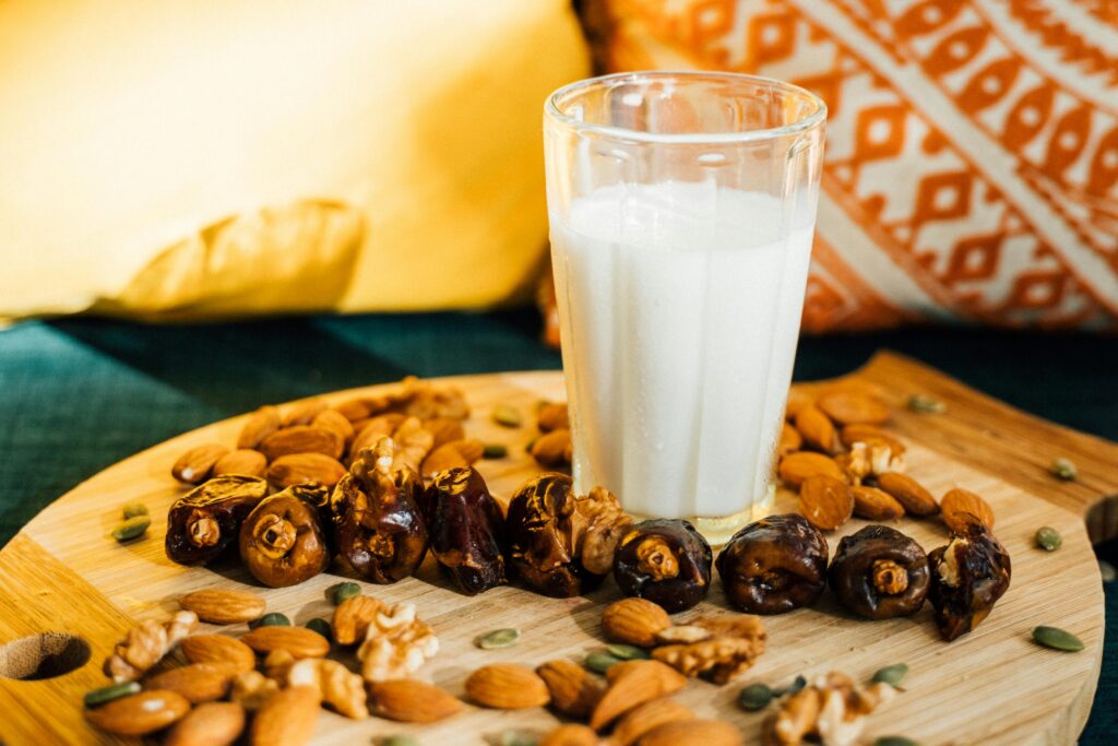 A refreshing glass of milk surrounded by dates, almonds, and nuts on a wooden board.