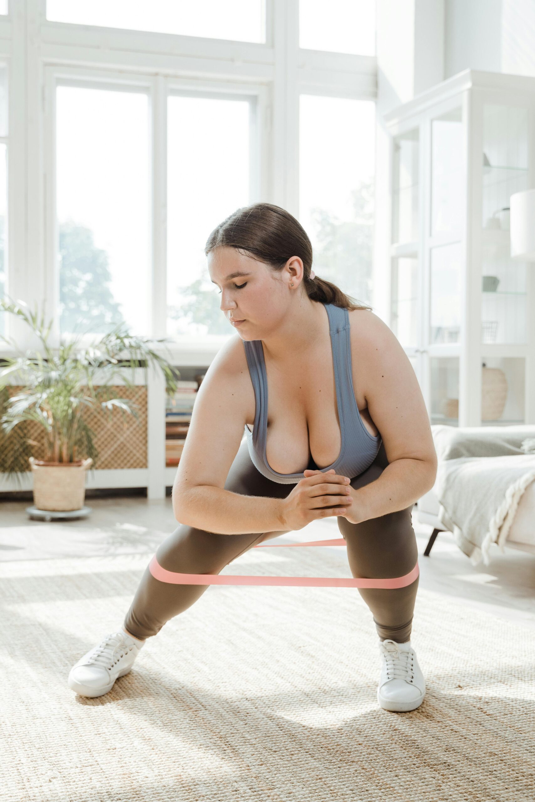Plus size woman performing a squat exercise with resistance band in a bright, modern room.