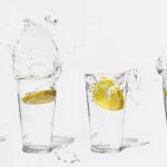 Four glasses with lemon slices creating splashes of water on a white background.