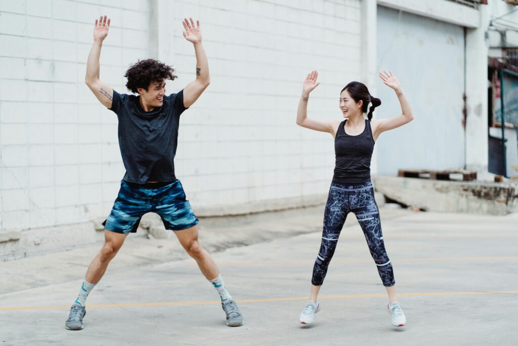 Dynamic young couple doing jumping jacks outdoors, embracing a fitness lifestyle.