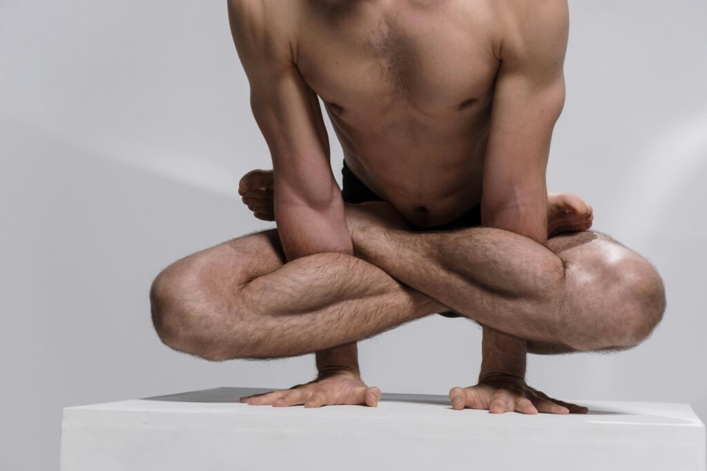 A shirtless man showcases flexibility and strength in a yoga contortion pose on a platform.