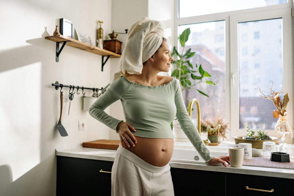 Young pregnant woman enjoys morning in kitchen, gazing outside.