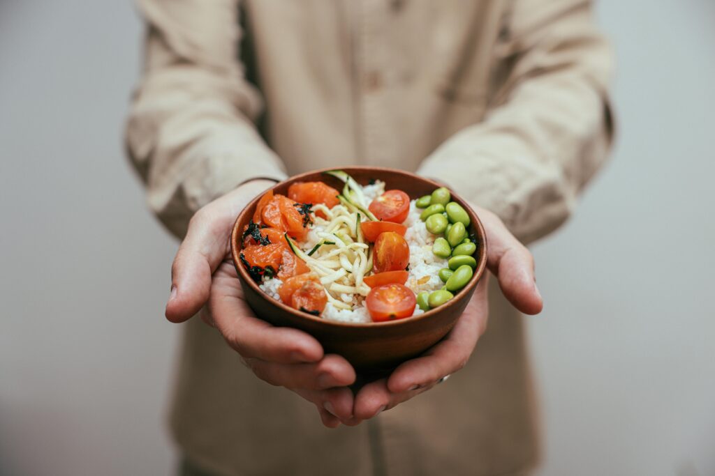 A nutritious bowl of rice topped with fresh vegetables held in hands.