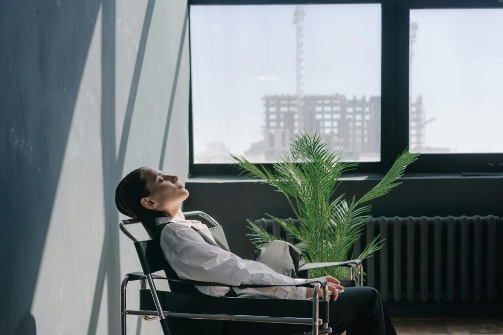 Woman in a minimalist office setting relaxing by the window with sunlight streaming in.