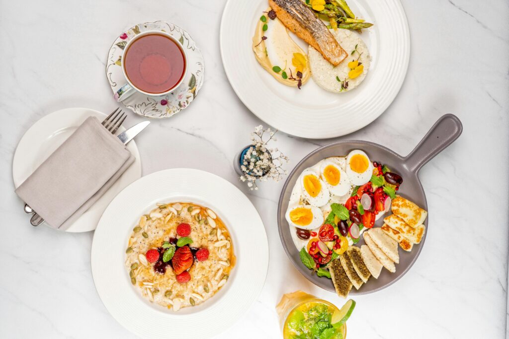 A delectable breakfast spread featuring oatmeal, poached salmon, eggs, vegetables, and tea on a white table.