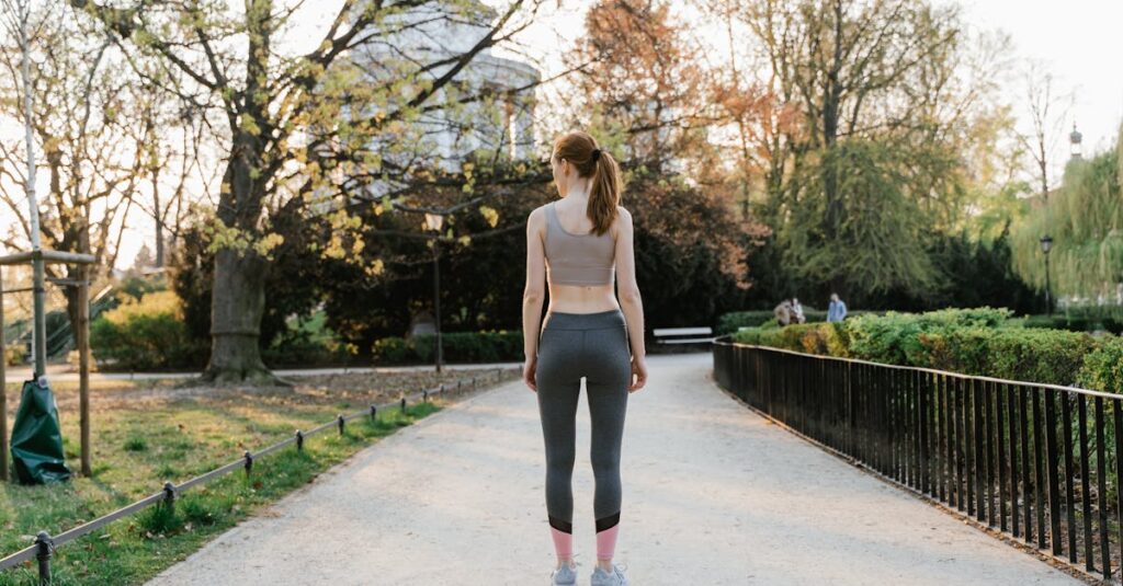 A woman in activewear walks along a path in a sunny park, showcasing fitness in nature.