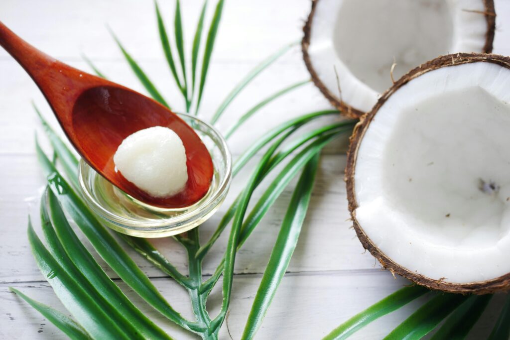 A close-up of organic coconut oil on a wooden spoon beside fresh coconut and palm leaves.