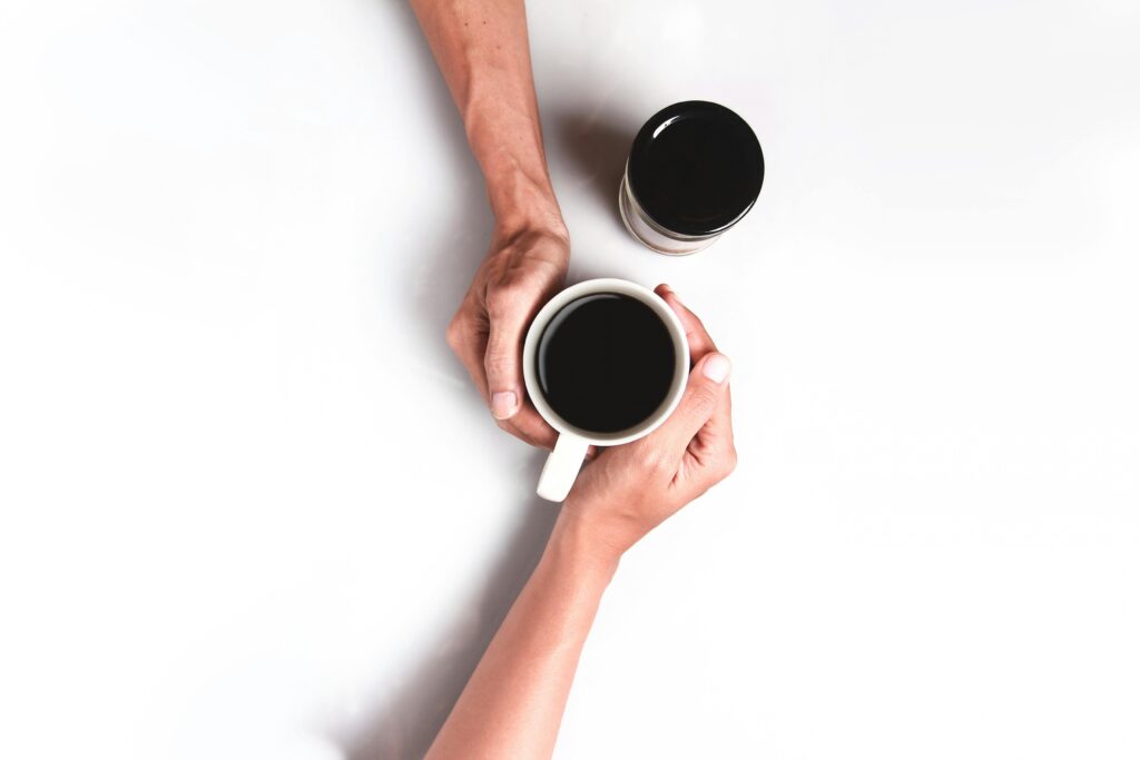 Minimalist top view of hands holding a black coffee cup on a white background.