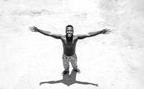 Black and white photo of a shirtless man smiling with arms spread wide, viewed from above.