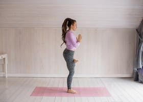 Side view of a woman doing yoga pose on mat indoors, embodying balance and fitness.