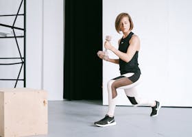 A young woman performing lunges with dumbbells in a modern indoor gym setting.