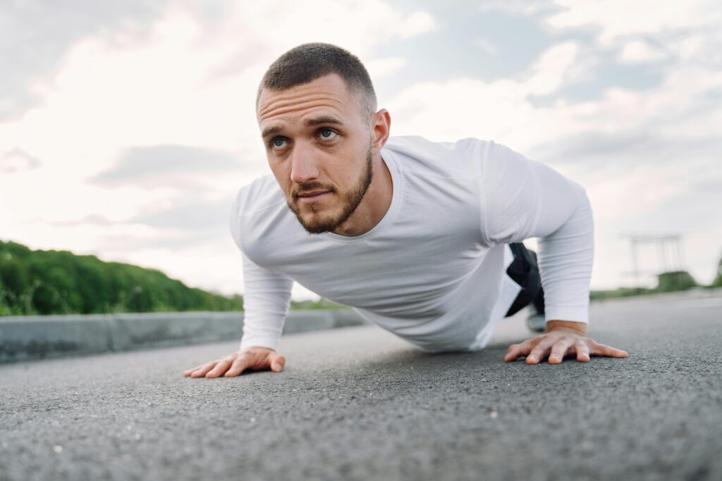 Focused man in sportswear doing push-ups on a road in a natural setting.