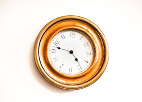 A stylish vintage wall clock with a golden frame and white face photographed against a bright white background.