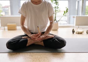 A man sits cross-legged holding an incense stick during yoga meditation indoors.