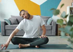 Adult man practicing yoga at home using a laptop for guidance. Relaxing indoor setting.