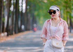 Stylish woman wearing sunglasses and visor cap walking on a tree-lined path in summer.