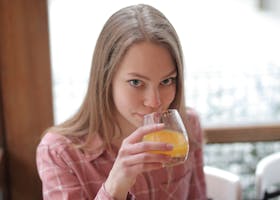 A young woman in a cozy indoor setting sips fresh orange juice, enjoying a relaxed moment.