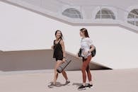 Two women in active wear walking outdoors while smiling and carrying yoga mats.