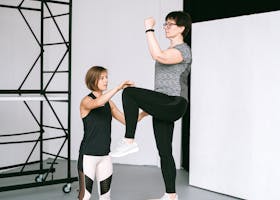 An elderly woman performs exercises with a fitness coach, focusing on a healthy lifestyle and wellness indoors.