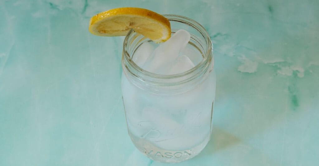 Close-up of a refreshing iced water in a mason jar with a lemon slice on a turquoise background, ideal for summer themes.