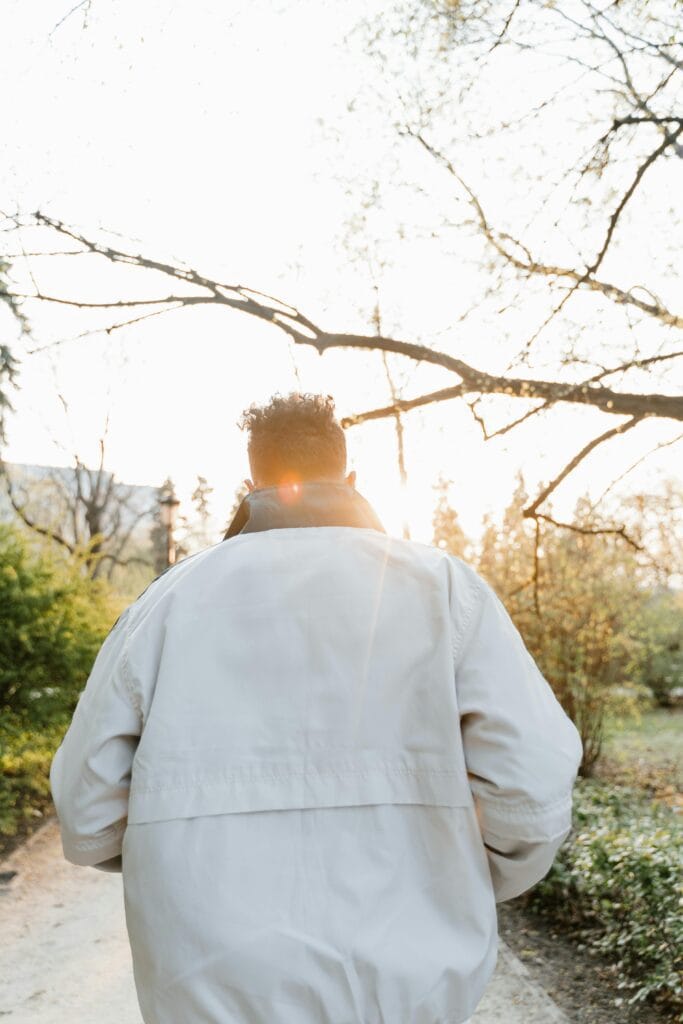 Rear view of a man walking through a park in sunlight, symbolizing wellness and active lifestyle.