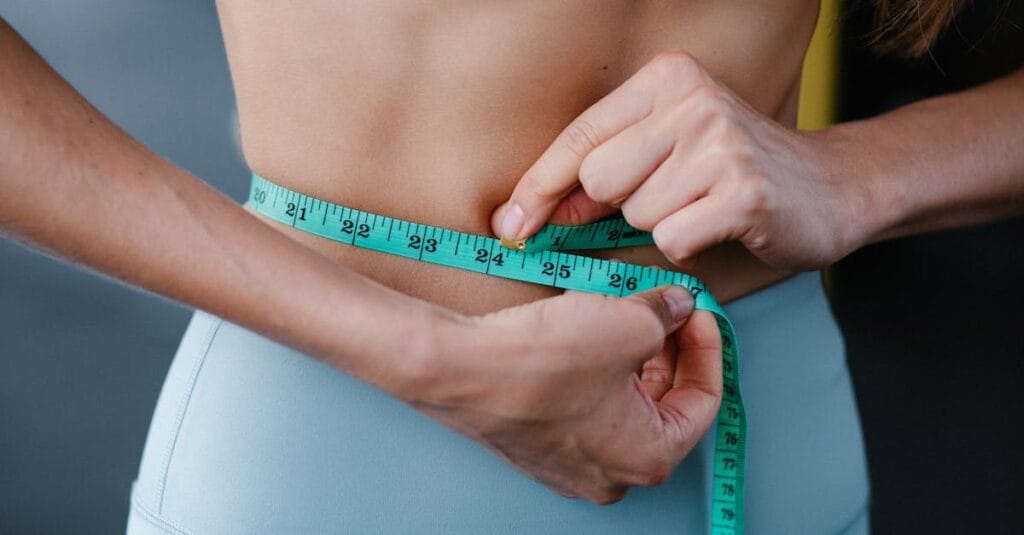 Close-up of a woman measuring her waist with a tape, representing fitness, health, and weight loss.