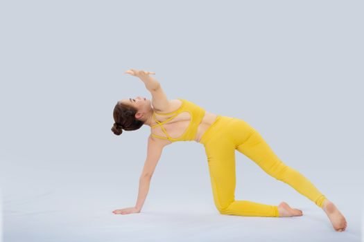 An Asian woman in vibrant sportswear performing yoga on a plain background.
