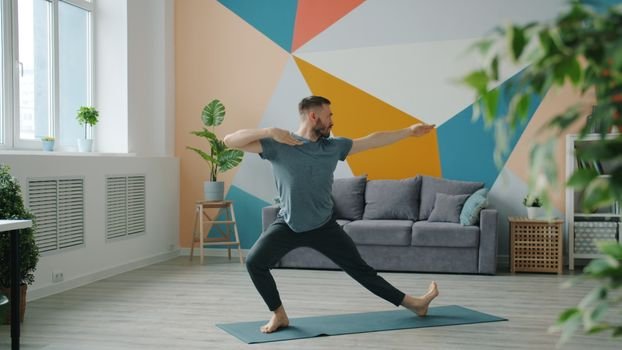 Adult man performing yoga in a stylish living room with geometric wall art.