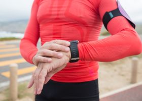 A person in red activewear checks their wristwatch during an outdoor exercise session.