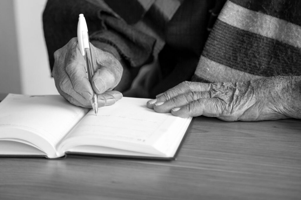 Close-up of elderly hands writing in a journal in monochrome. Captures a moment of reflection.