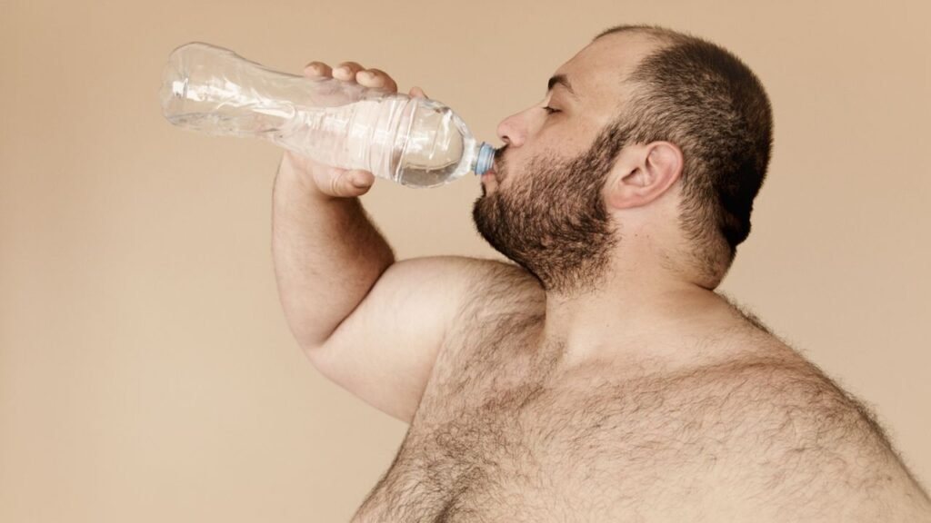 Bearded man drinking water from plastic bottle to stay hydrated and healthy.