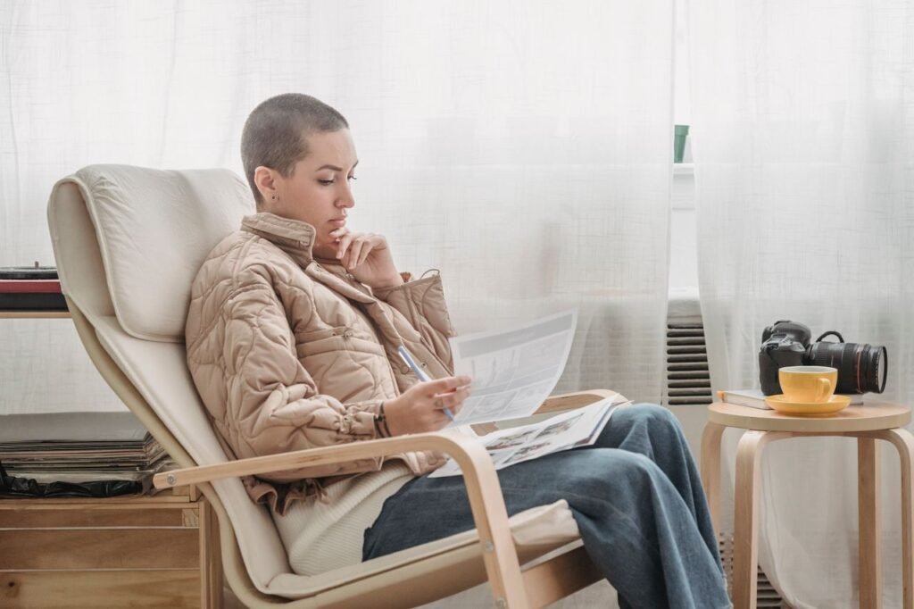 A woman in a cozy chair reading a newspaper in a bright, airy room.
