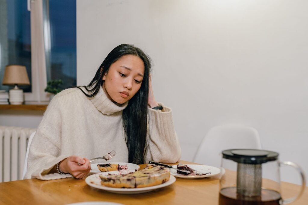 A thoughtful woman in a cozy sweater eats dessert alone, reflecting deep thoughts.