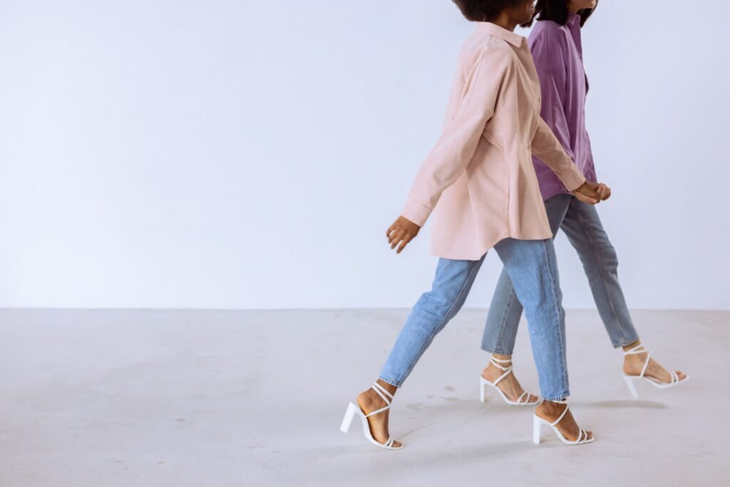 Two women in trendy attire walking against a white background showing modern fashion sense.
