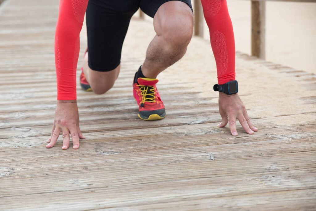 Athlete in red gear gets ready to sprint on a wooden path in sunny outdoor setting.