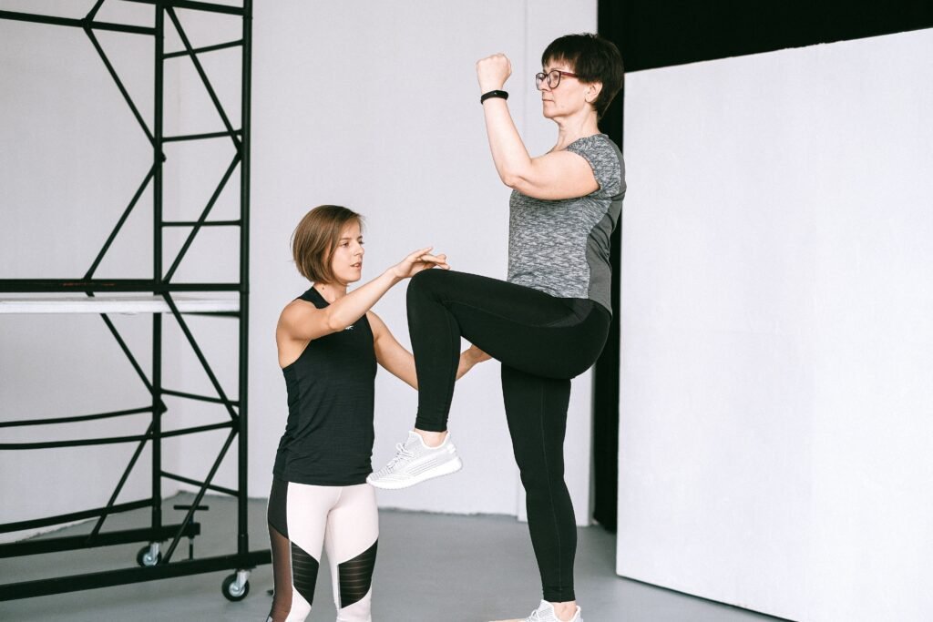 An elderly woman performs exercises with a fitness coach, focusing on a healthy lifestyle and wellness indoors.